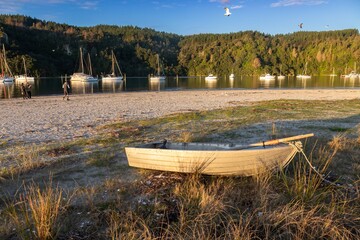A small aluminum boat with oars rests on the sandy shore of Whangamata, Coromandel Peninsula, New...