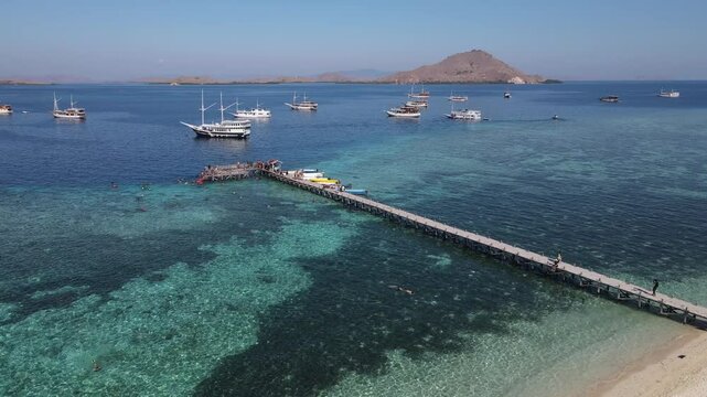 Aerial drone view of Kanawa Island beach with long bridge dock and sailing boats around.