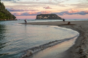 Fishermen cast lines at sunset on a beach. Others walk along the shore, while one digs in the sand....
