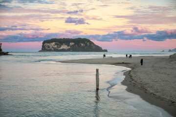 People stroll along the beach at sunset in Whangamata, Coromandel Peninsula, New Zealand. The...