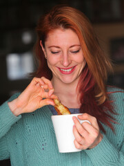Happy redhead woman enjoying coffee and croissants in a cozy indoor setting.