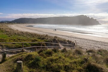 A family walks along the beach in Whangamata, New Zealand. The group enjoys the sunshine and ocean...