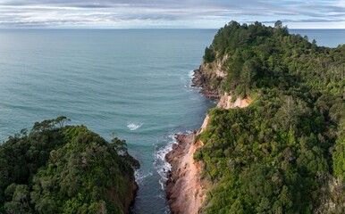 Aerial view of a rugged coastline with lush green forest meeting the turquoise ocean in Whiritoa,...