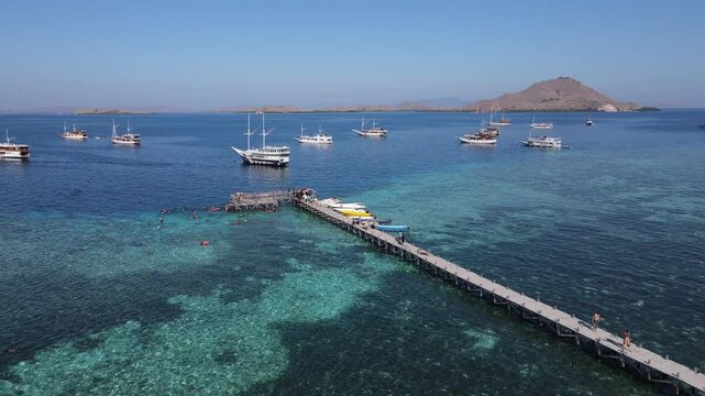 Aerial drone view of Kanawa Island beach with long bridge dock and sailing boats around.