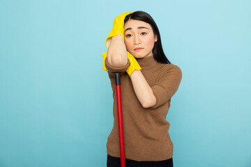 Fatigued asian housemaid leans on broomstick, looking worn out and disheartened after long hours of...