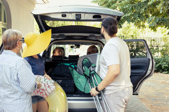 Family of three generations smiling as they load their packed car for a trip to the seaside, exploration and adventure. Large group excited about the road trip journey, bonding and togetherness.