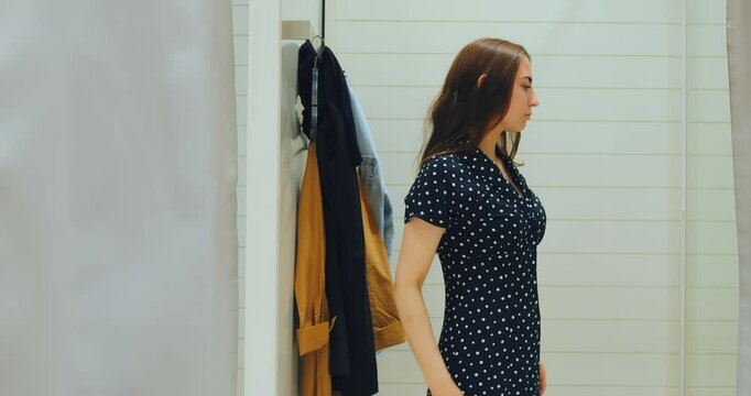 Woman stepping into frame pushing curtain aside to showcase outfit, outfit reveal repeated in elegant gesture, curtain folds accentuating outfit styling moment in modern fitting room setting
