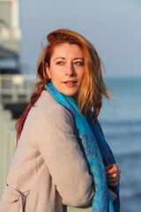 Obraz premium Close-up of redhead woman in autumn clothing standing outside, on pier lost in thought.