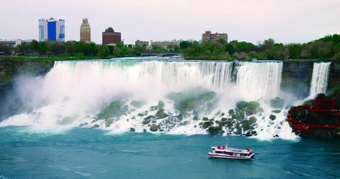 Daytime view of Niagara Falls crest with boat tour passing below, mist cloud hovering over river, cinematic scene conveying Canada-US border cliffs and powerful waterfall rim under clear sky.