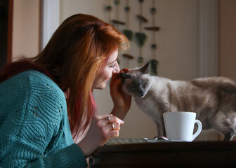 Cozy indoor scene with ginger-haired woman, 30s, sitting at table in home wear. Having breakfast...