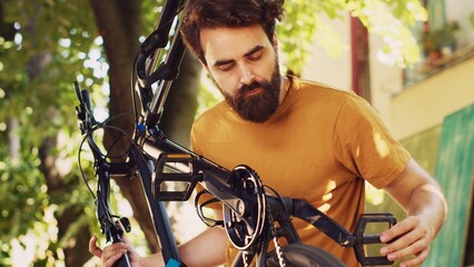 Detailed view showing athletic caucasian man attentively adjusting and realigning bicycle pedal and crank arm. Close-up view of youthful male doing maintenance on bike components in yard.