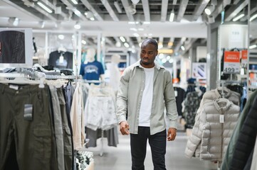 Customer choosing clothes in fashion store, concentrated man shopping in retail mall