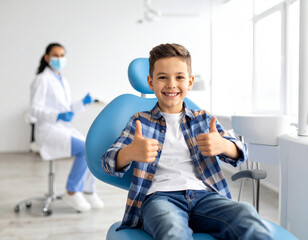 Happy child in dental chair smiling and showing thumbs up with pediatric dentist in background during dental visit