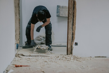 A young man collects construction waste with a dustpan.