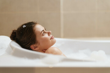 Naklejka premium Serene young woman relaxing in a luxurious bubble bath, enjoying a moment of tranquility and self-care. Spa and wellness concept with soft lighting.