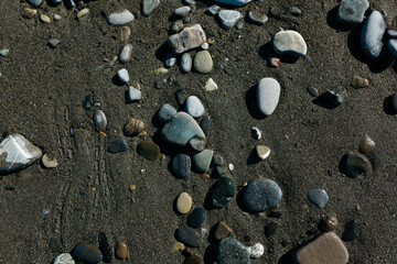 glossy stones washed by the sea wave shine from the rays of the sun on a summer day. pebbles on the city beach.the concept of environmental protection from pollution by petroleum products and plastics