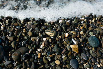 glossy stones washed by the sea wave shine from the rays of the sun on a summer day. pebbles on the city beach.the concept of environmental protection from pollution by petroleum products and plastics