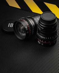 Detailed close-up of two camera lenses placed on a dark, textured surface. Yellow and black caution...
