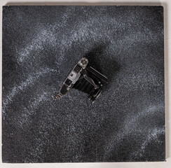 An old camera rests on a textured black surface, showcasing its vintage design. The scene reflects...