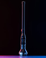A modern flashlight stands upright on a surface, illuminated with red and blue lights, creating a striking visual contrast against the dark backdrop.