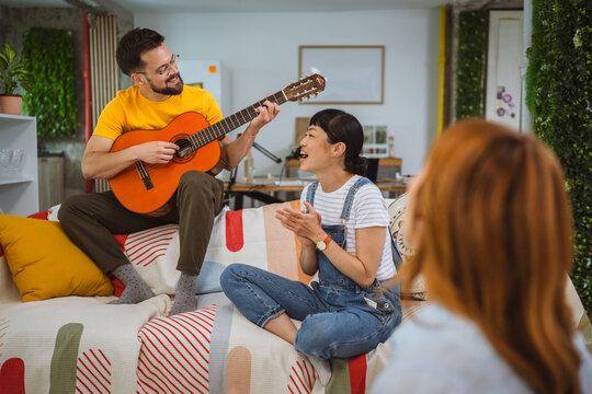 Caucasian man sit on sofa and play guitar for his female friends