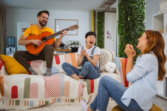 Caucasian man sit on sofa and play guitar for his female friends