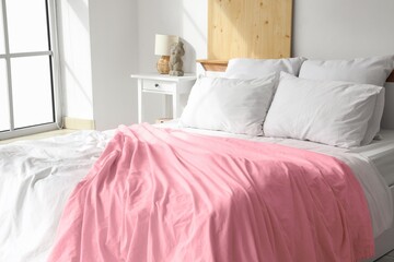Cozy bed with soft pillows and pink blanket near window in light bedroom