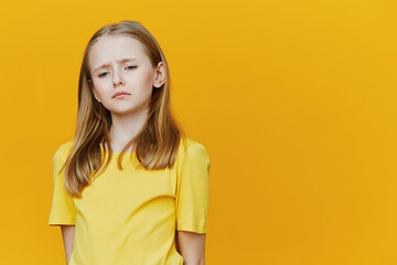 Sad little girl in a yellow t shirt against a vibrant yellow background, expressing feelings of...