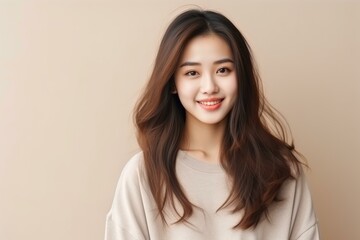 Studio portrait of a cheerful young asian woman with long brown hair, wearing a casual beige shirt and smiling gently