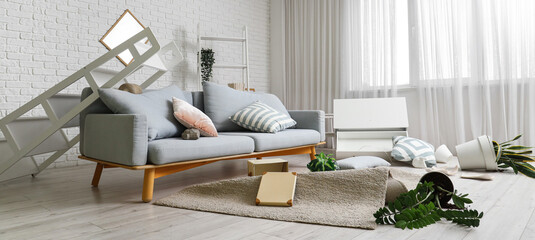 Interior of messy living room with sofa and overturned things after earthquake