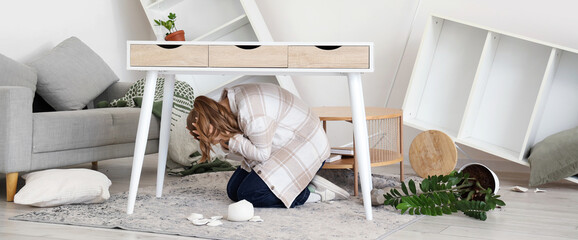 Scared woman hiding under table at home during earthquake