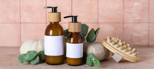 Composition with bottles of shampoo, bath sponges and green twigs on table near pink tile wall