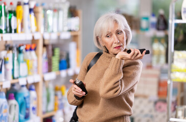 Attentive old woman reviewing different scents to buy in shop with large stock