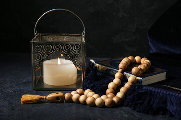 Muslim lamp with burning candle, prayer beads and Koran on dark background