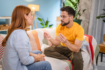 Caucasian stressed couple sitting on couch, arguing at home.