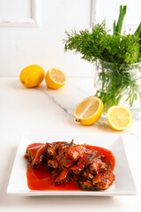 Plate with canned fish in tomato sauce and lemons on white table