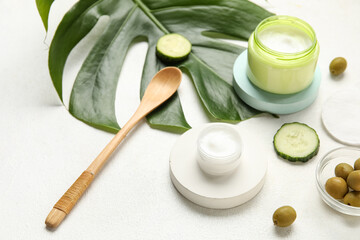 Composition with jars of natural cream, ingredients and palm leaf on light background