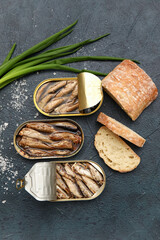 Opened tin cans with sprats in oil, green onion and bread on black table