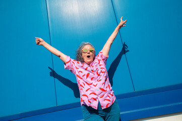 Excited mature woman celebrating with arms raised against blue background
