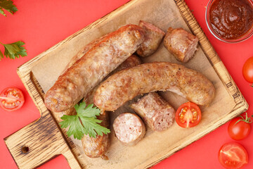 Wooden board of tasty homemade sausages with sauce on red background