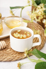 Cup of linden tea and bowl with honey on white table