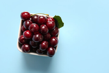 Bowl with sweet cherries and leaf on blue background