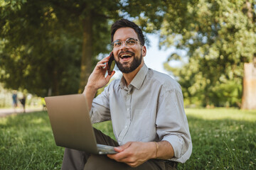 smiling businessman sit on grass in nature talk on mobile phone
