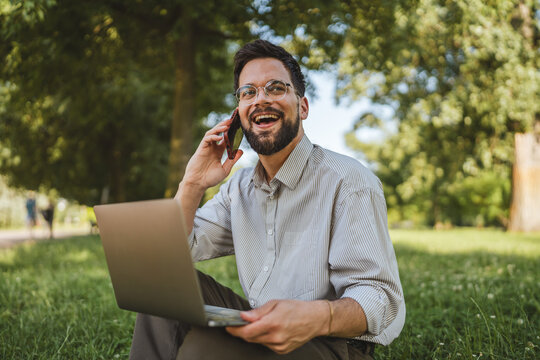 smiling businessman sit on grass in nature talk on mobile phone