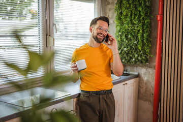 cheerful adult man drink coffee and have a phone call in the kitchen