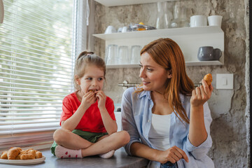Caucasian mother and little daughter having a bite in kitchen together
