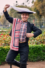 Portrait of a smiling, cheerful young man dressed as a Chilean huaso, celebrating and posing to...