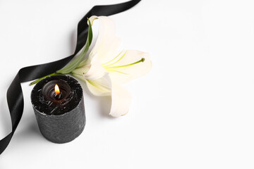 Beautiful lily flower with burning candle and black funeral ribbon on white background