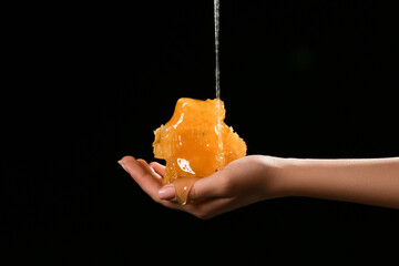 Female hand with sweet honeycombs on black background
