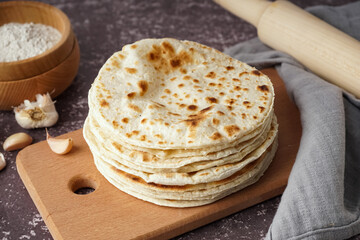 Wooden board of tasty pita bread on grey background